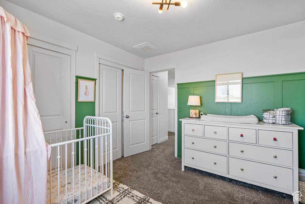 Bedroom with dark colored carpet, a nursery area, a closet, and wainscoting