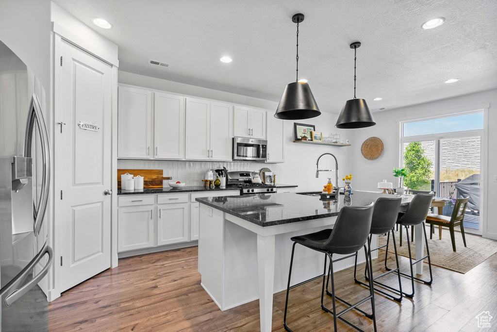 Kitchen featuring stainless steel appliances, a sink, white cabinetry, wood finished floors, and a kitchen island with sink