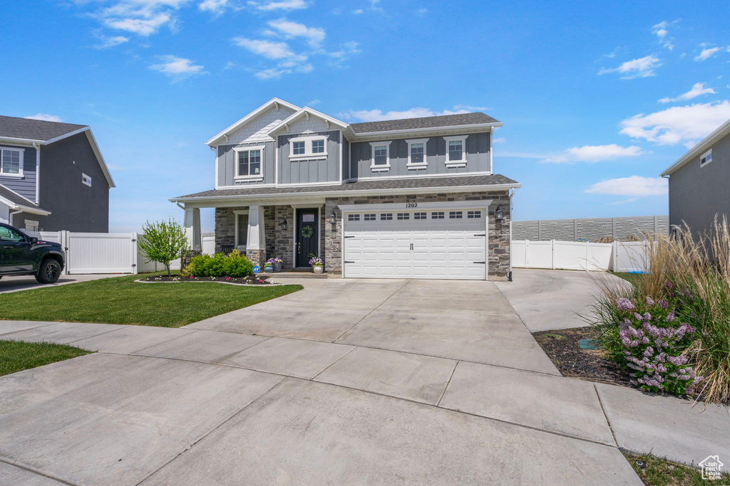 View of front facade with driveway, stone siding, an attached garage, and board and batten siding