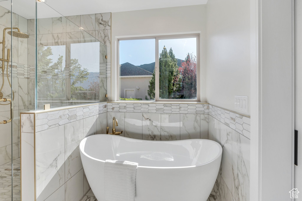 Bathroom with tile walls, a stall shower, a freestanding bath, and a wainscoted wall