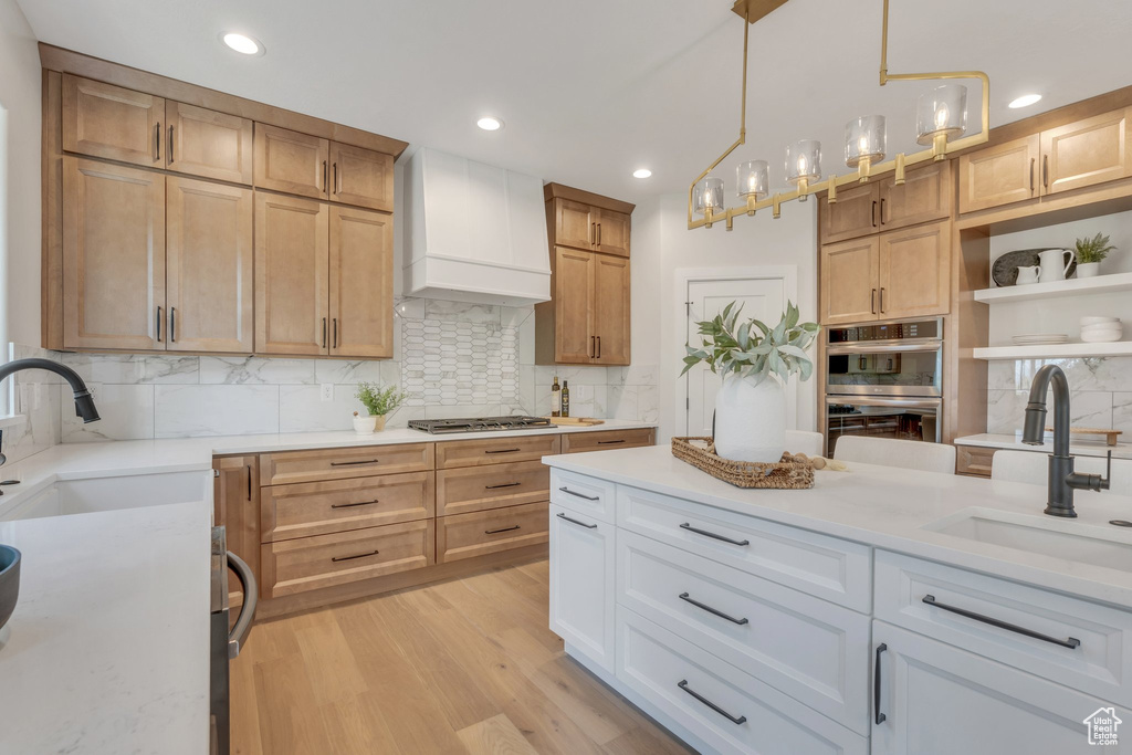 Kitchen with custom range hood, a sink, appliances with stainless steel finishes, light wood-type flooring, and recessed lighting