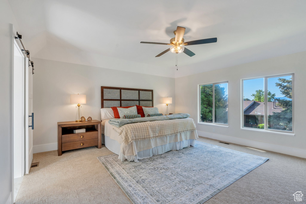 Bedroom featuring light colored carpet, baseboards, a barn door, and ceiling fan