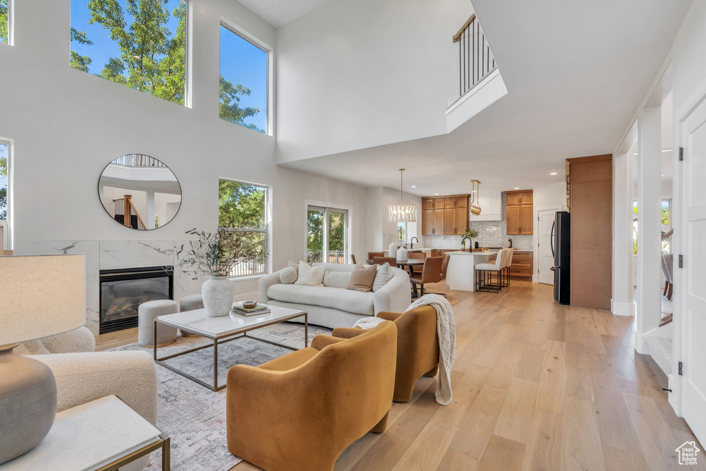 Living room with light wood-type flooring, a fireplace, a towering ceiling, recessed lighting, and a chandelier