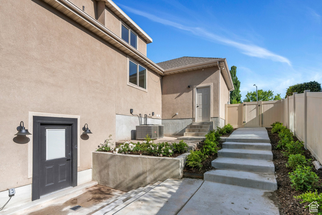 Property entrance with a gate, cooling unit, fence, stucco siding, and a patio
