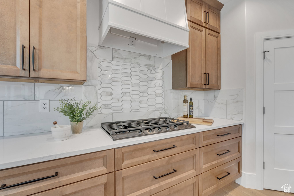 Kitchen featuring stainless steel gas cooktop, custom range hood, light countertops, and tasteful backsplash