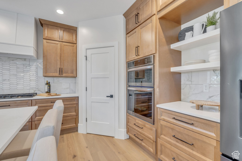 Kitchen with appliances with stainless steel finishes, open shelves, light wood-type flooring, light countertops, and decorative backsplash