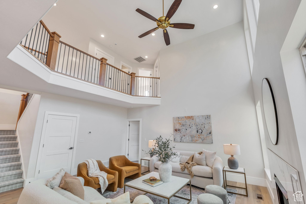 Living room featuring a high ceiling, ceiling fan, stairway, wood finished floors, and recessed lighting