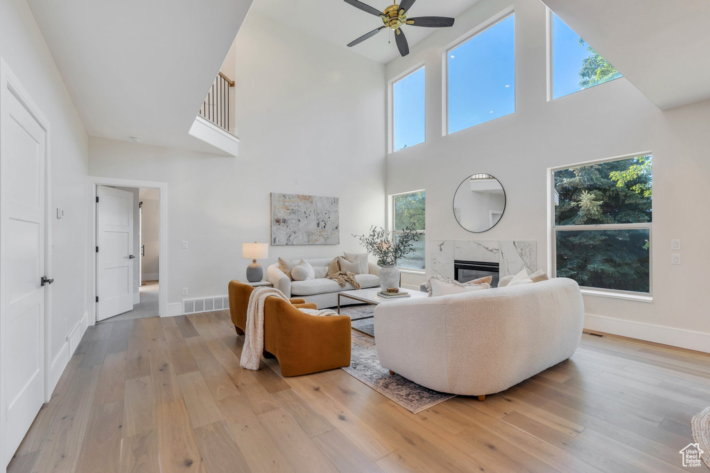 Living area with a high ceiling, ceiling fan, a premium fireplace, light wood finished floors, and baseboards
