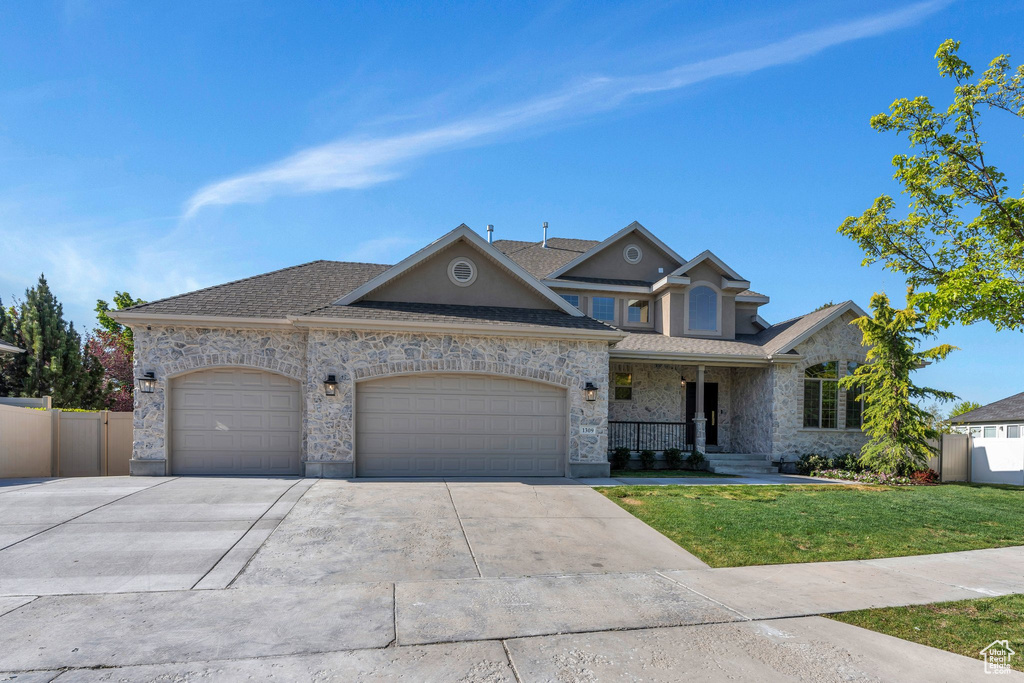 View of front facade with a garage, driveway, covered porch, stone siding, and roof with shingles