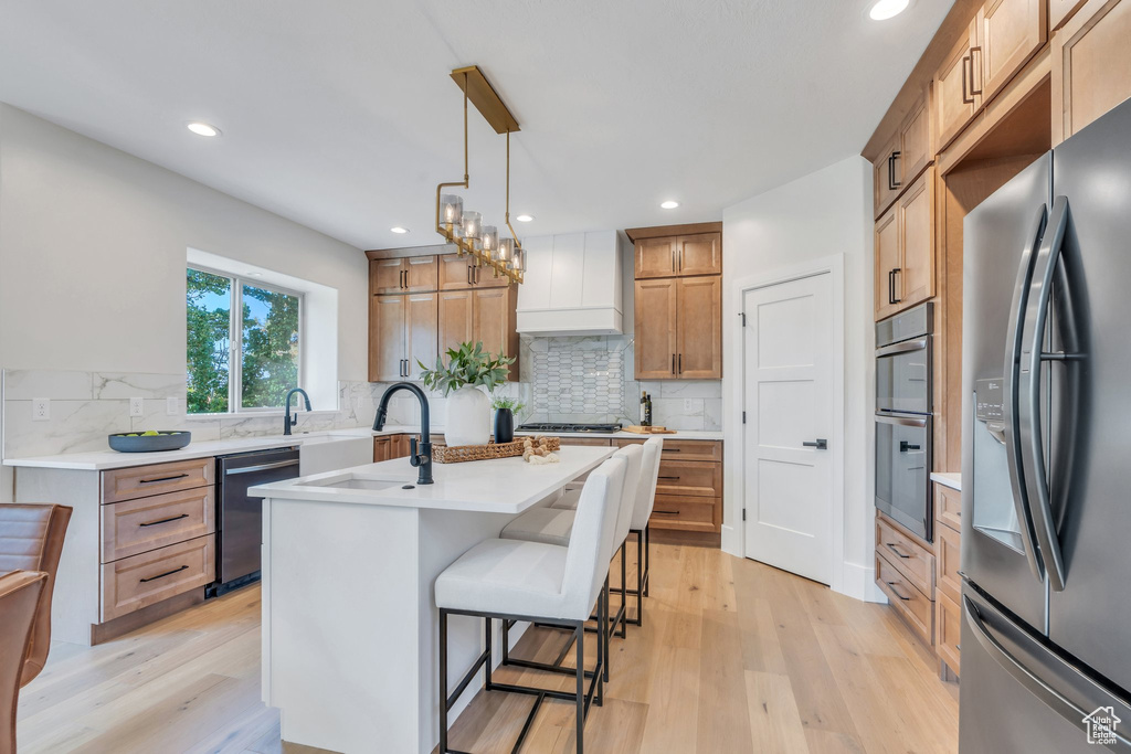 Kitchen featuring appliances with stainless steel finishes, light wood-style floors, custom exhaust hood, recessed lighting, and a breakfast bar area