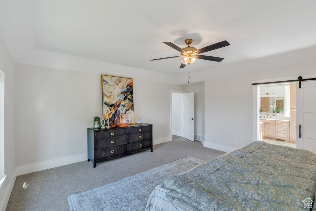 Bedroom with carpet flooring, a barn door, baseboards, ensuite bath, and ceiling fan