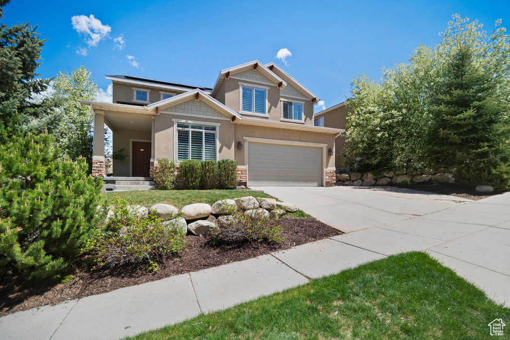Craftsman-style house featuring stone siding, driveway, roof mounted solar panels, and an attached garage
