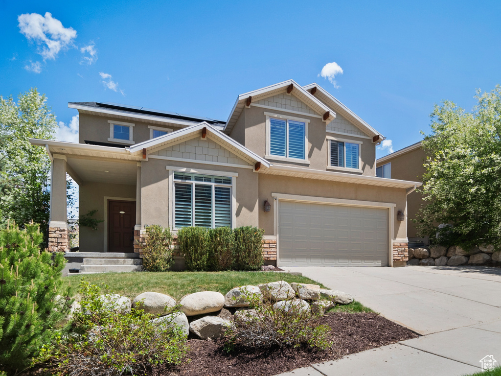 Craftsman-style house featuring stone siding, driveway, roof mounted solar panels, and an attached garage