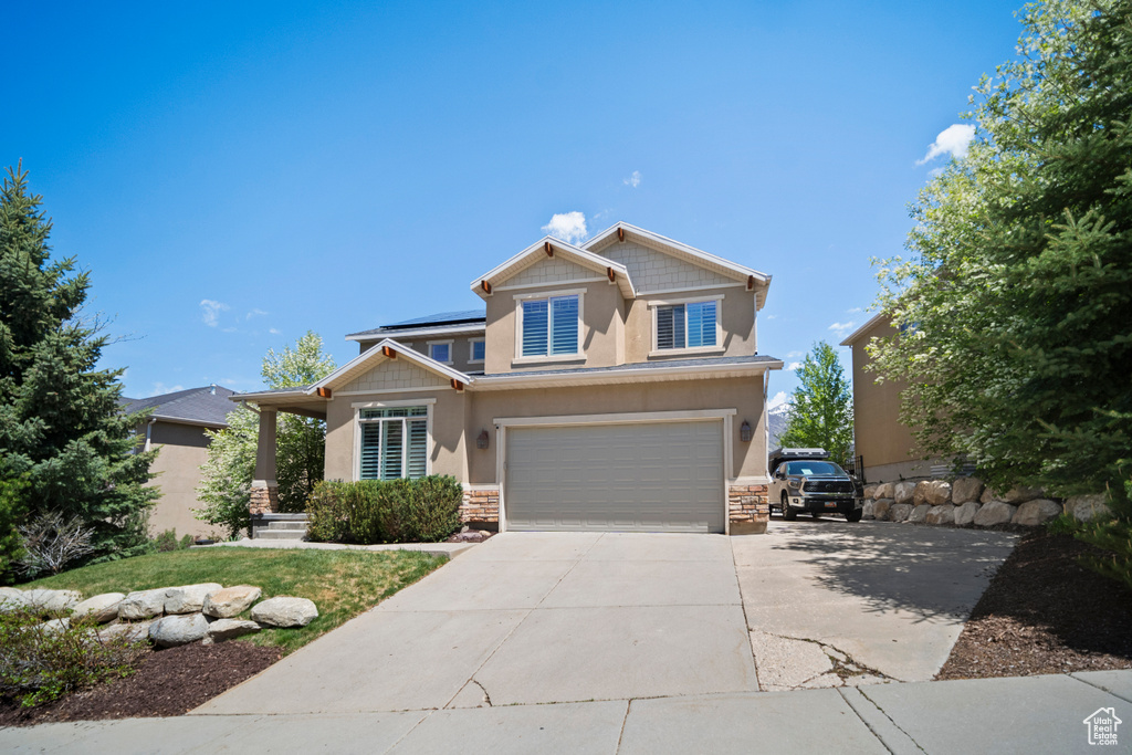Craftsman house with stone siding, roof mounted solar panels, a garage, concrete driveway, and stucco siding