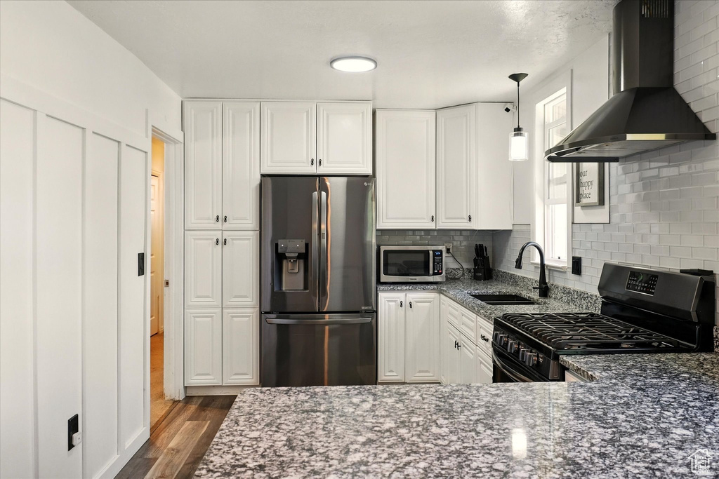 Kitchen with appliances with stainless steel finishes, ventilation hood, a sink, and dark stone countertops