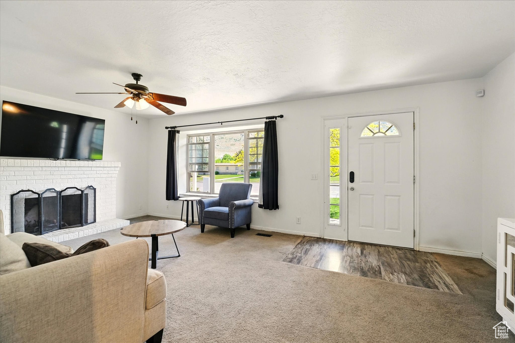 Carpeted living room with a ceiling fan, baseboards, and a brick fireplace
