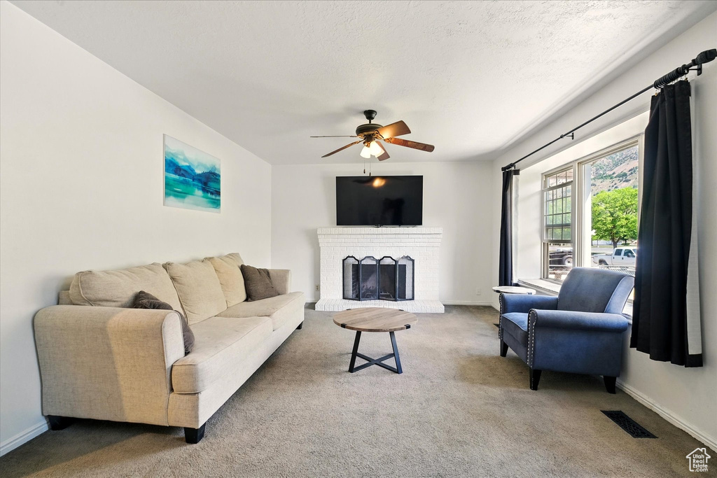 Living room with a ceiling fan, carpet flooring, a brick fireplace, baseboards, and a textured ceiling
