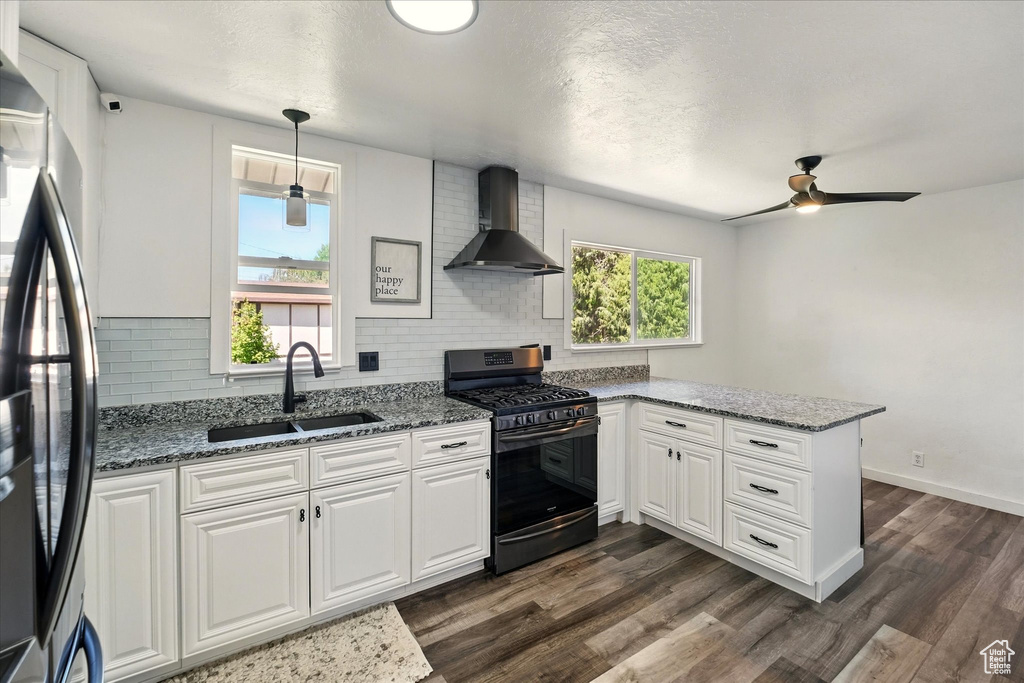 Kitchen with gas range oven, wall chimney exhaust hood, a sink, freestanding refrigerator, and a peninsula
