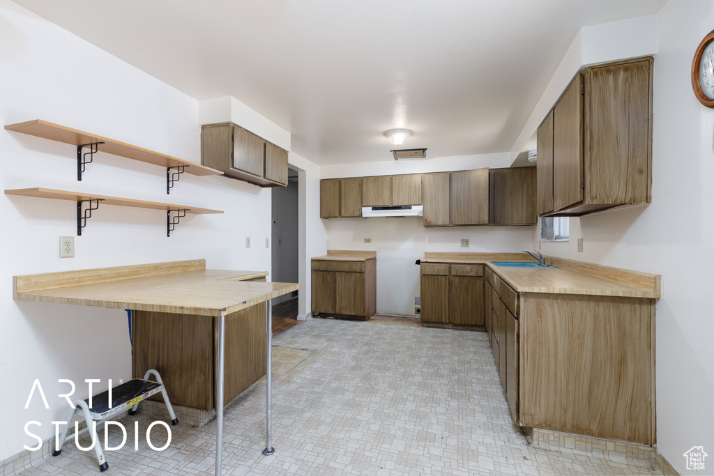 Kitchen with open shelves, under cabinet range hood, a sink, a peninsula, and light countertops