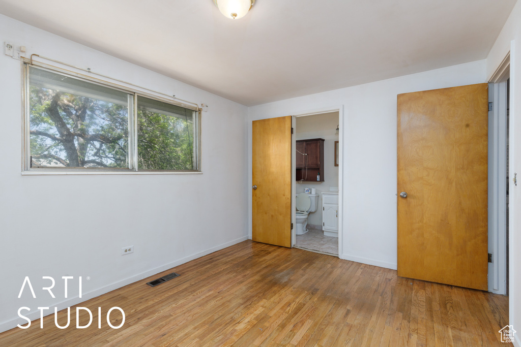 Unfurnished bedroom with light wood-style flooring, baseboards, and connected bathroom