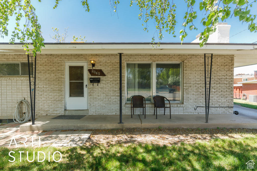 Doorway to property with a chimney, brick siding, and covered porch