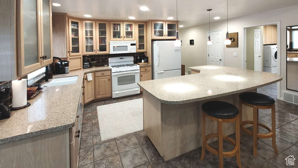 Kitchen featuring white appliances, a center island, a breakfast bar, recessed lighting, and washer / clothes dryer