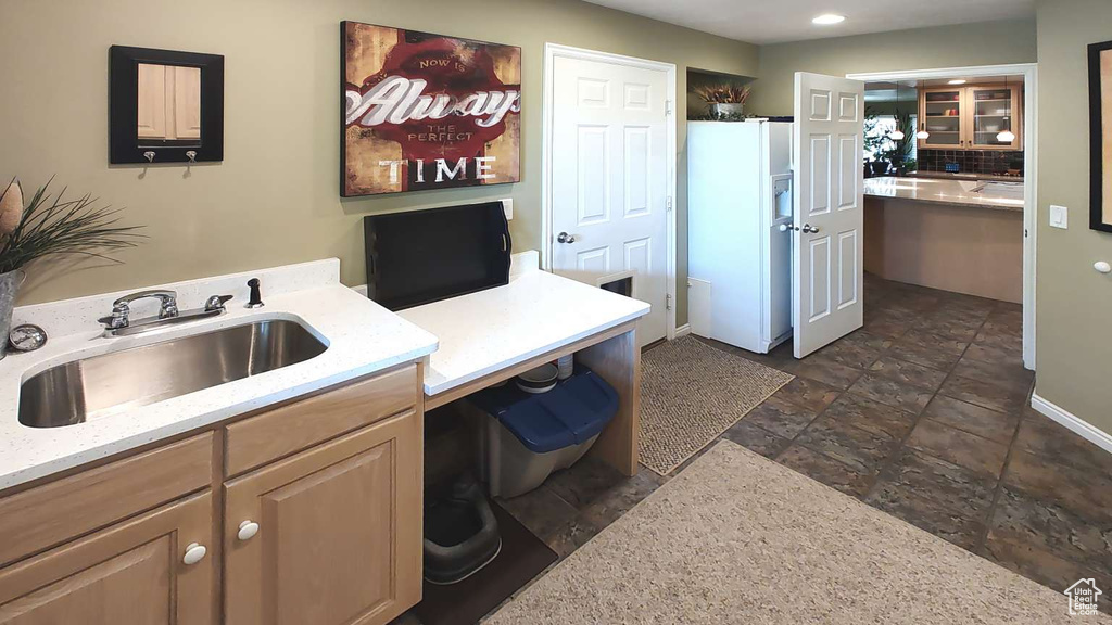 Kitchen featuring white fridge with ice dispenser, a sink, stone tile floors, an office area, and light stone counters