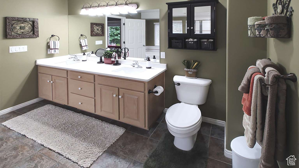 Full bathroom featuring toilet, double vanity, and baseboards
