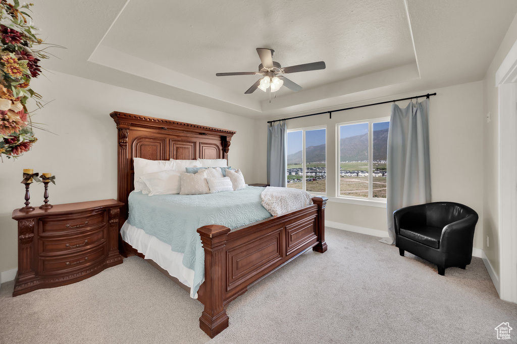 Bedroom featuring a raised ceiling, light carpet, baseboards, a mountain view, and a ceiling fan