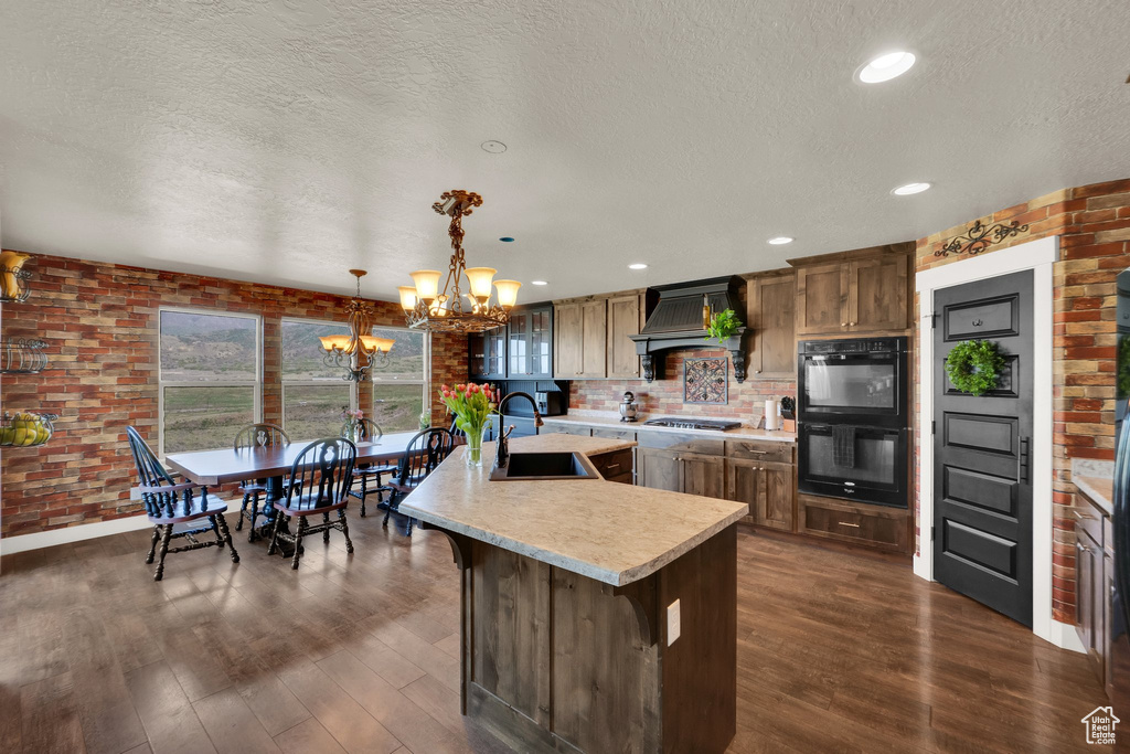 Kitchen with a chandelier, light countertops, a sink, dark wood-style flooring, and brick wall