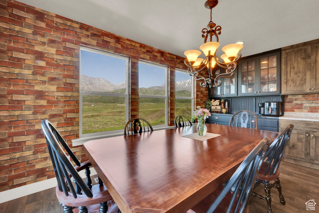 Dining area with a chandelier, dark wood-style floors, a mountain view, and brick wall