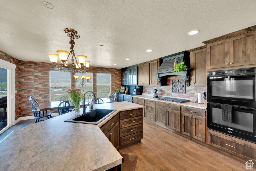 Kitchen with a sink, premium range hood, a chandelier, light wood-style floors, and a textured ceiling