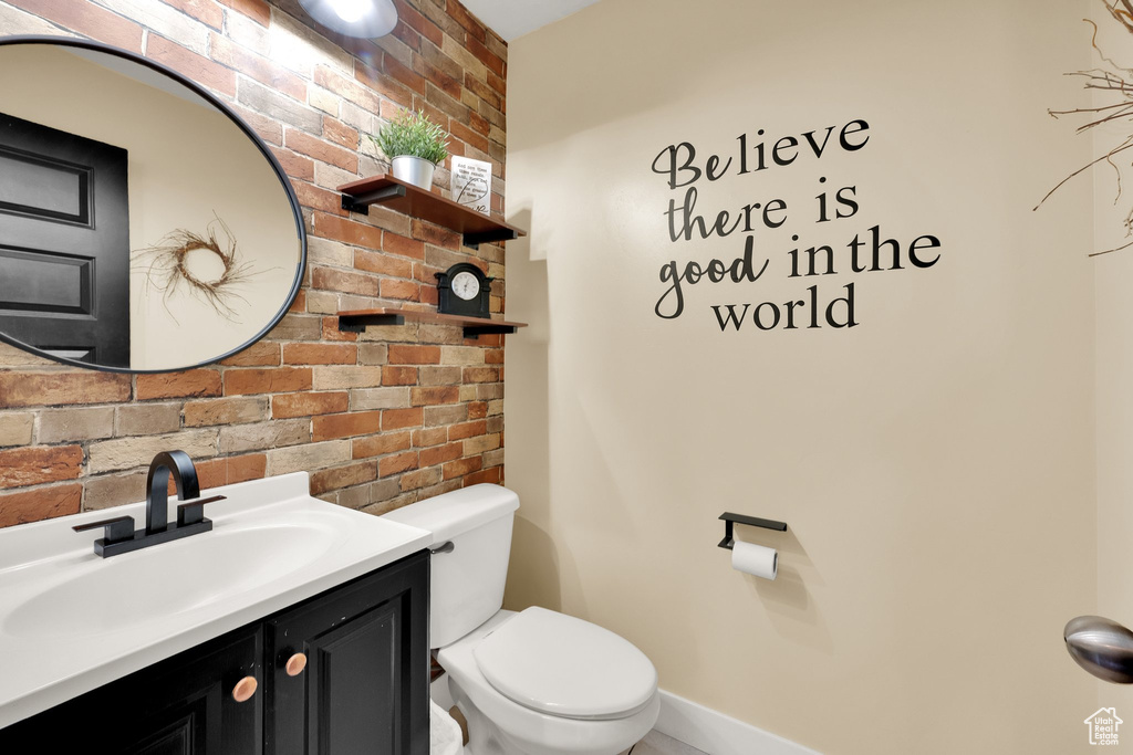 Bathroom featuring brick wall, toilet, vanity, and baseboards