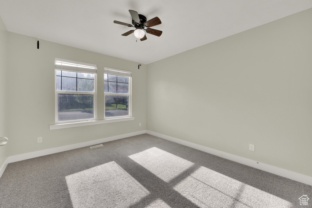Carpeted empty room featuring a ceiling fan and baseboards