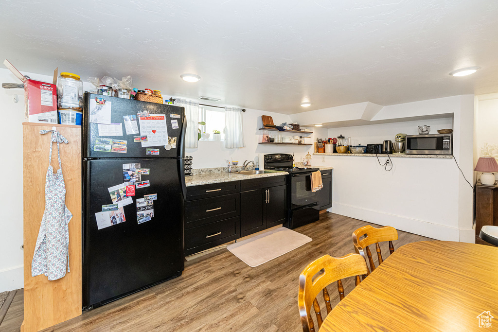 Kitchen featuring black appliances, dark cabinets, light wood-style flooring, a sink, and light countertops