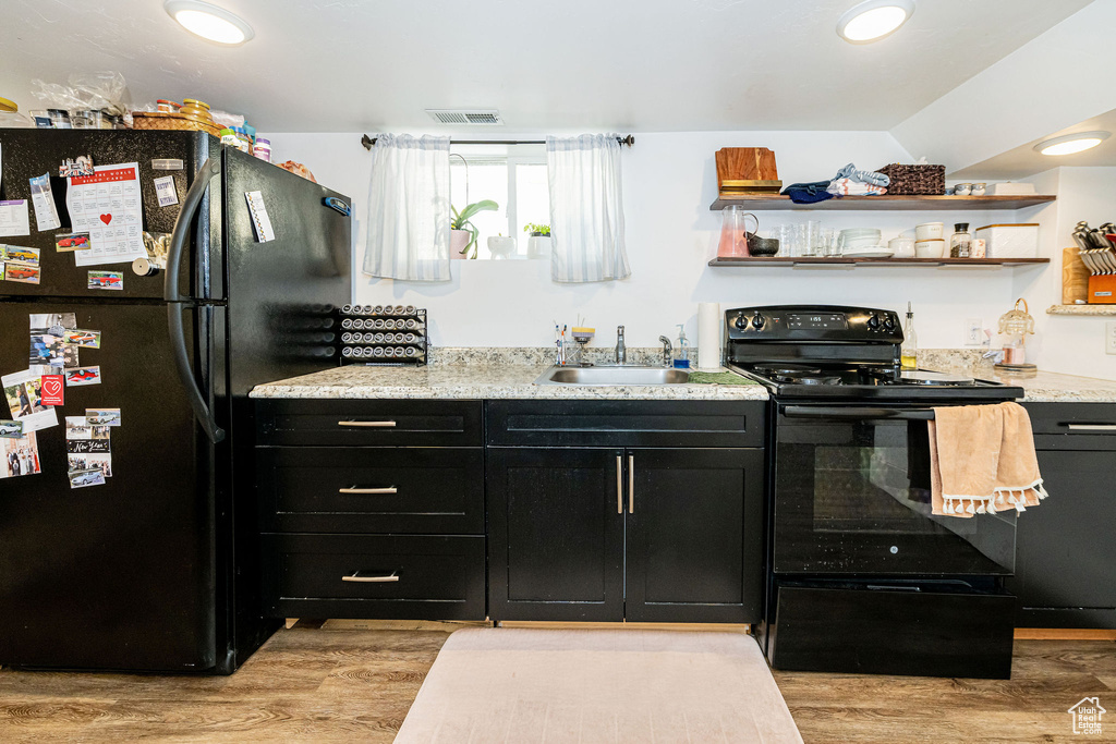Kitchen with black appliances, dark cabinetry, a sink, light wood-style floors, and open shelves