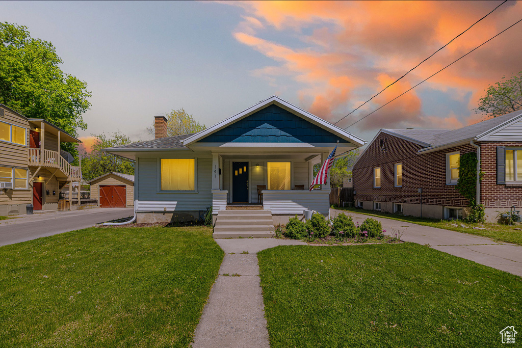 Bungalow featuring a porch, a chimney, an outdoor structure, a front lawn, and a detached garage
