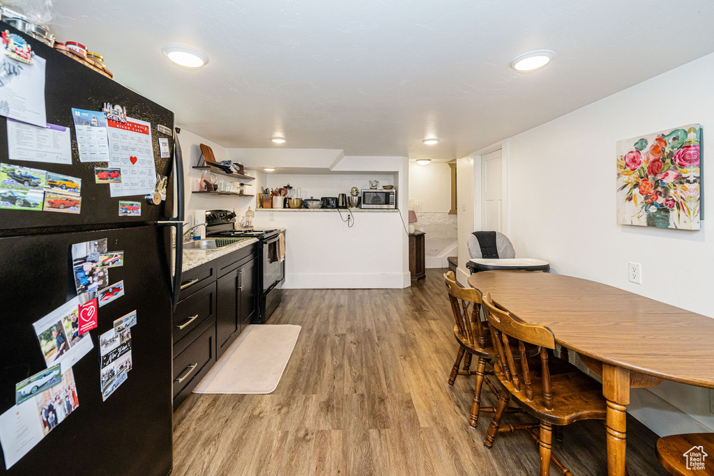 Kitchen featuring black appliances, light wood finished floors, open shelves, light countertops, and dark cabinetry
