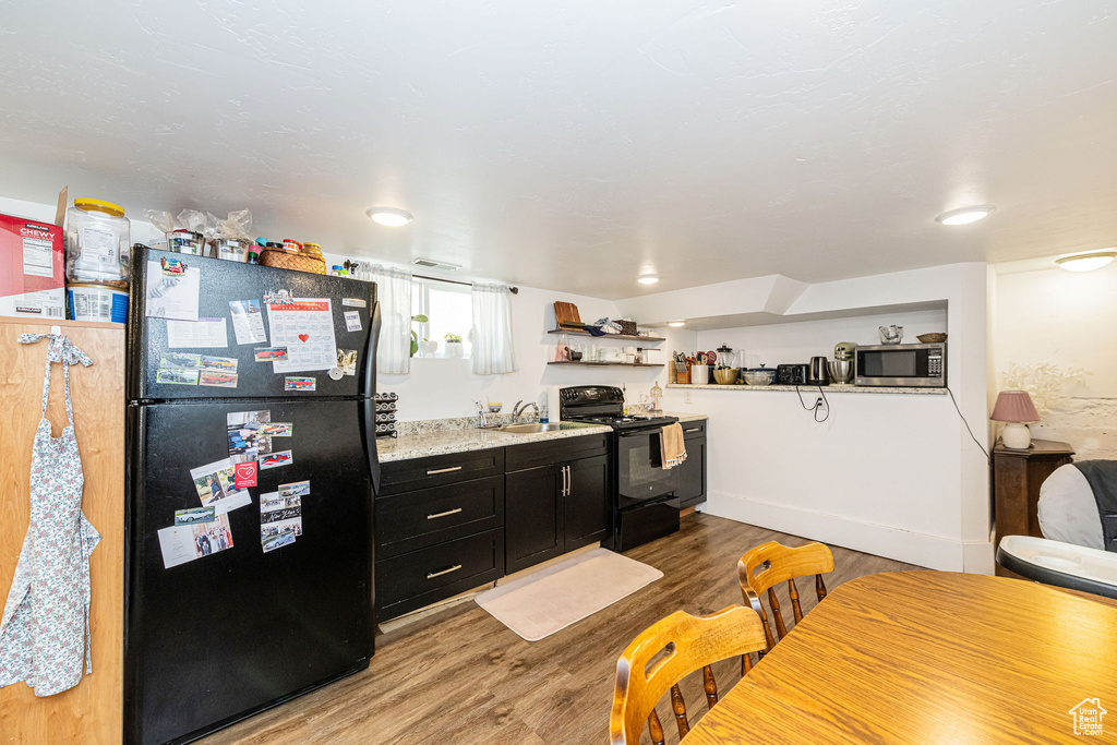 Kitchen featuring black appliances, dark cabinetry, light wood-type flooring, a sink, and open shelves