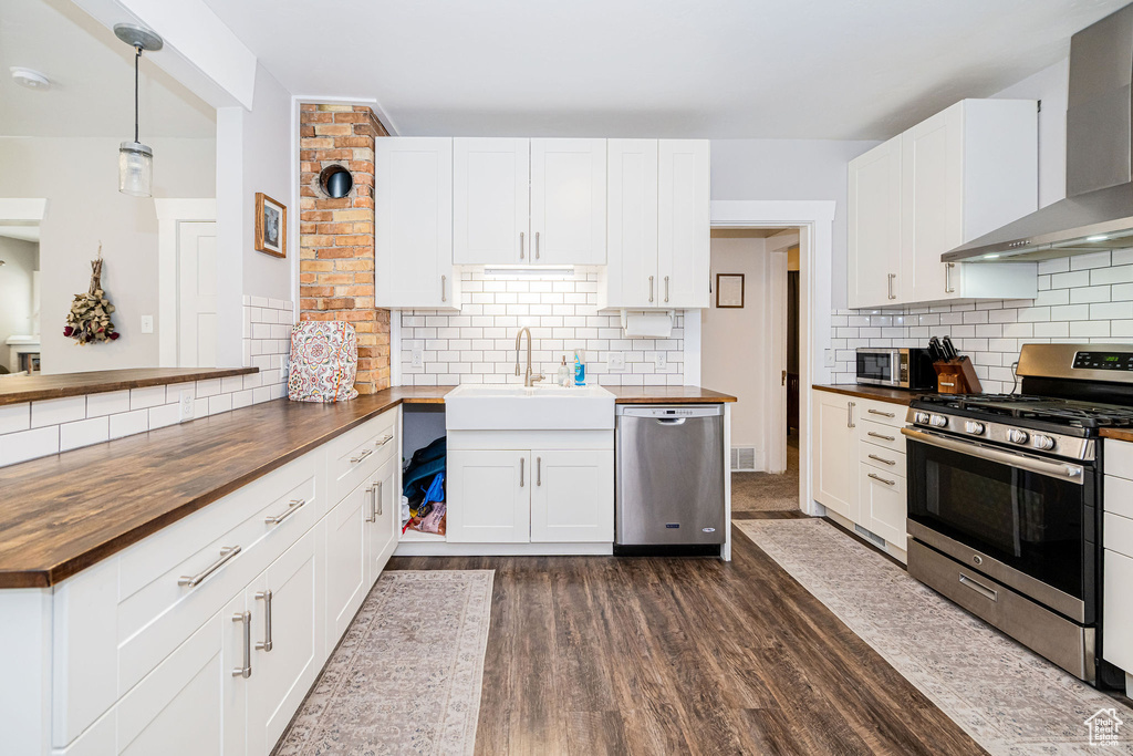 Kitchen with wood counters, appliances with stainless steel finishes, wall chimney range hood, a sink, and tasteful backsplash