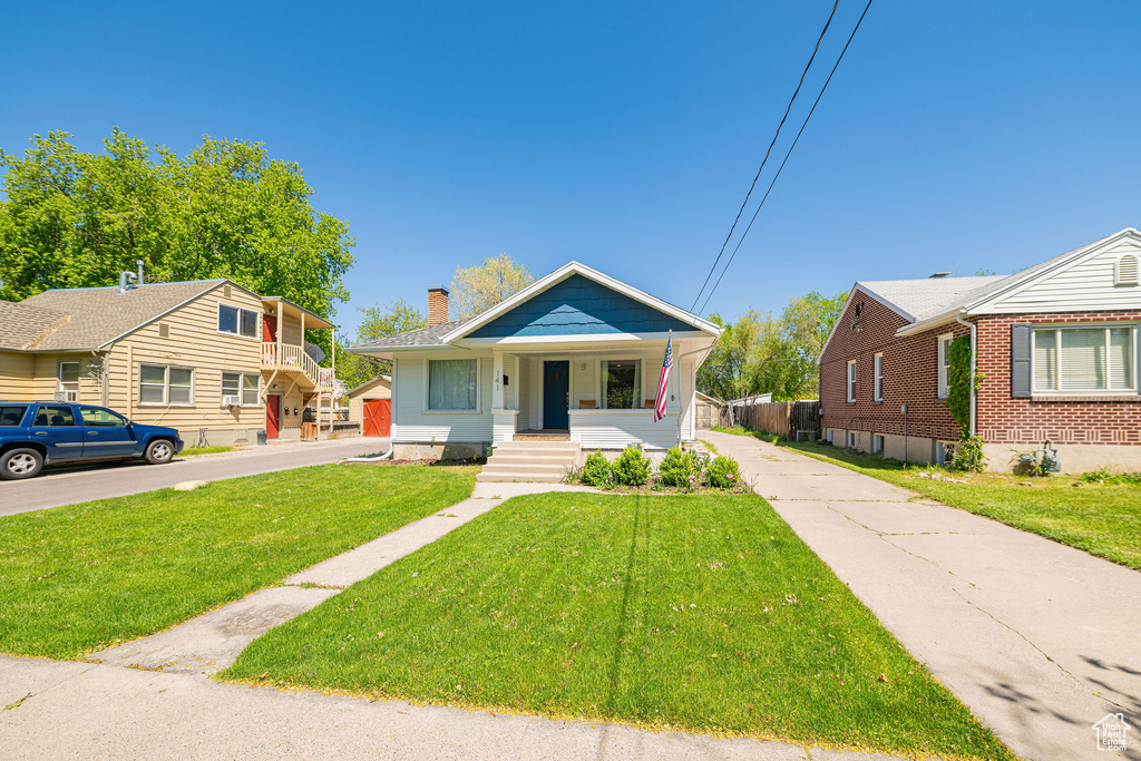 Bungalow with covered porch, a chimney, a front lawn, and driveway
