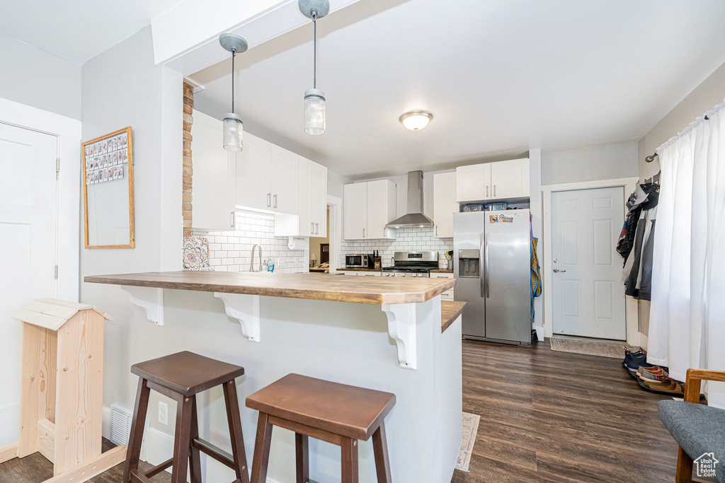 Kitchen featuring stainless steel appliances, wall chimney exhaust hood, butcher block countertops, and dark wood-style floors