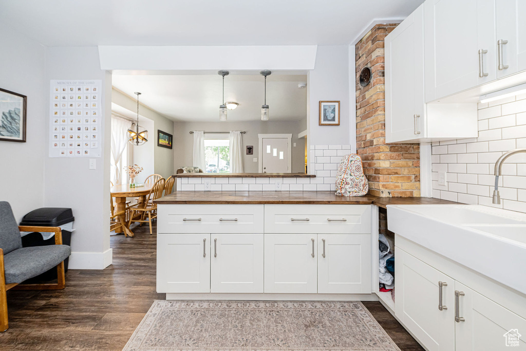 Kitchen with butcher block counters, dark wood-style flooring, decorative backsplash, white cabinets, and a peninsula