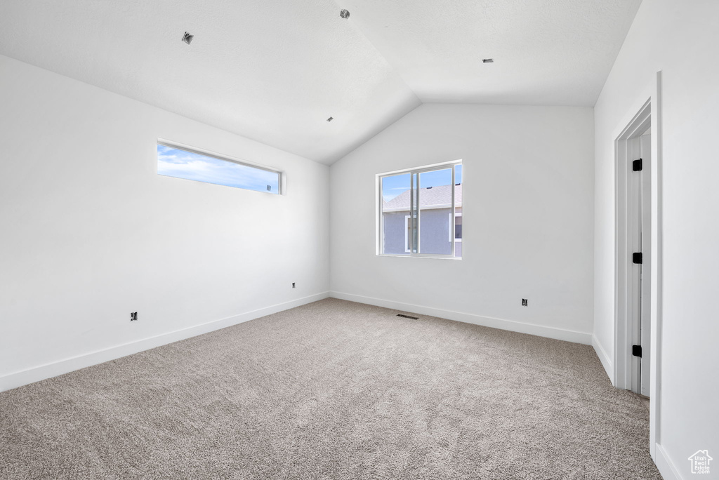Carpeted spare room with vaulted ceiling and baseboards