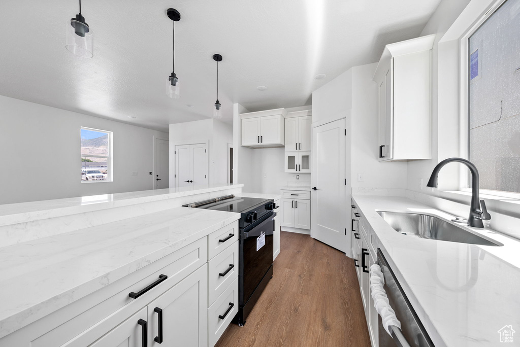 Kitchen featuring electric range, light stone counters, wood finished floors, and white cabinets