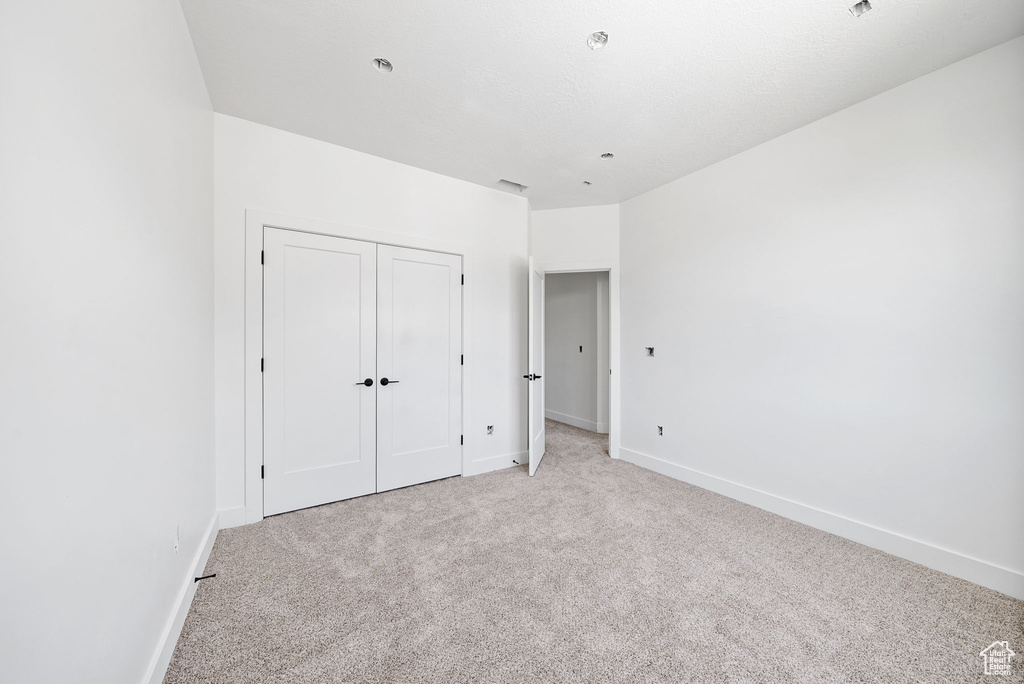 Unfurnished bedroom featuring light carpet and a closet