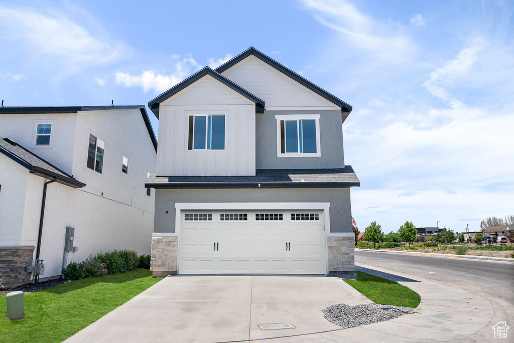 View of front of home featuring stone siding, concrete driveway, a garage, a shingled roof, and board and batten siding