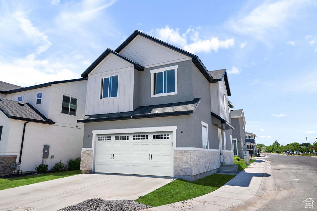 View of front of property with stone siding, an attached garage, concrete driveway, board and batten siding, and roof with shingles