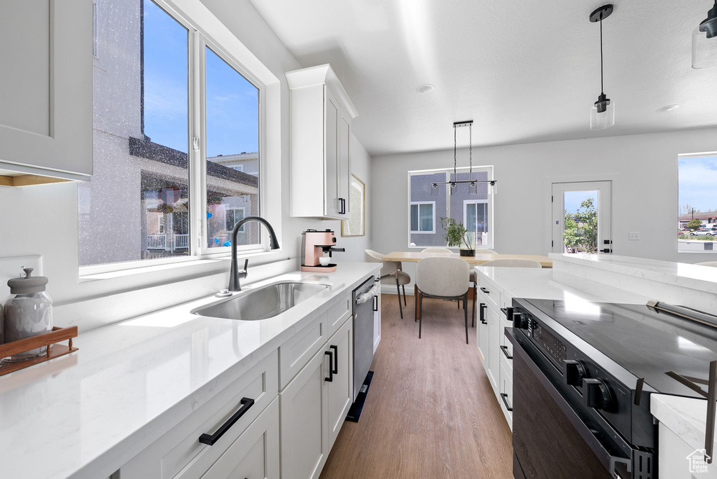 Kitchen featuring decorative light fixtures, dishwasher, light wood-style floors, white cabinets, and black electric range