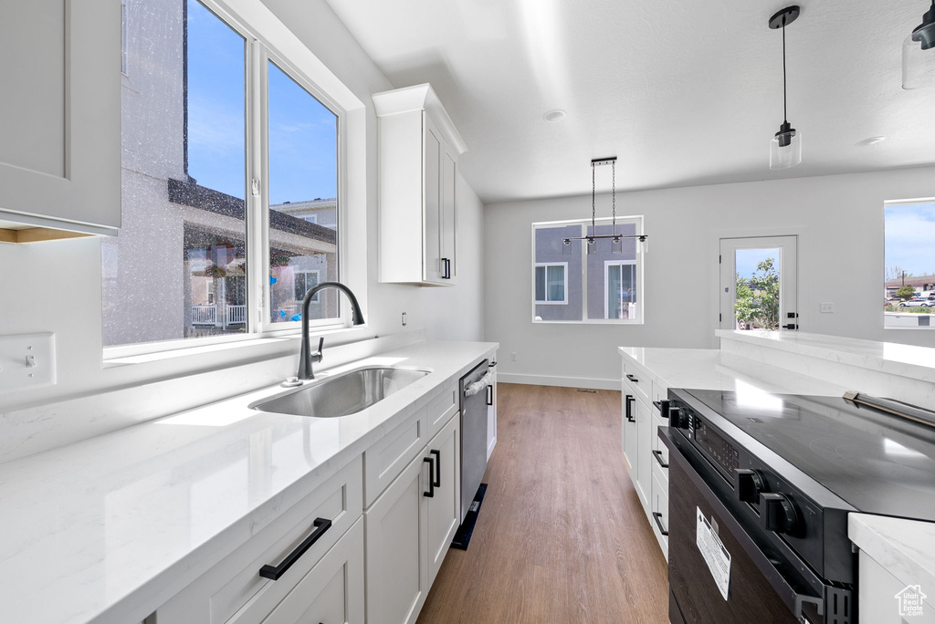 Kitchen featuring black electric range, hanging light fixtures, light wood-type flooring, white cabinets, and dishwasher